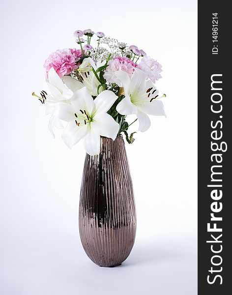 A flower arrangement of carnations and lillies in a brown metallic vase. A flower arrangement of carnations and lillies in a brown metallic vase