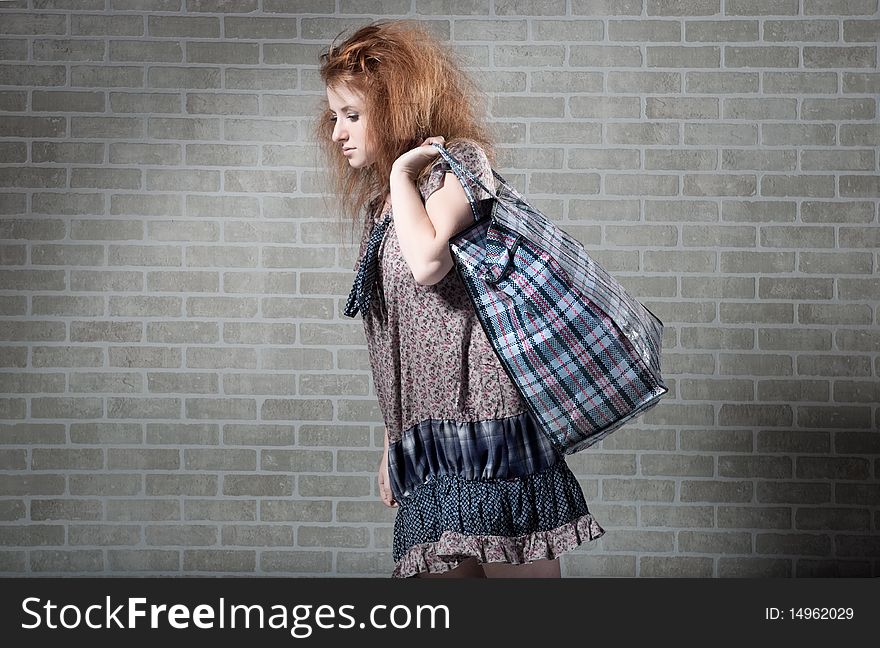 Tired redhaired woman with shopping bag.  brick wall as background.
