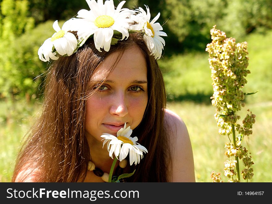 Charming young woman in garland white field camomile upon green meadow