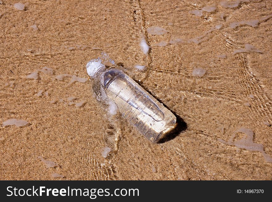 A bottle of water thrown on the shore of the ocean and is washed by waves