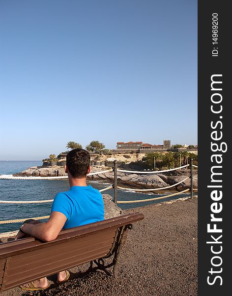 Young man sitting alone on a bench and looking out to the ocean. Young man sitting alone on a bench and looking out to the ocean