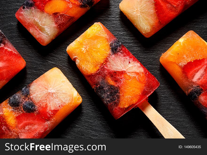 Fruit popsicles, homemade fruit ice lolly of various fruits with the addition of citrus lemonade on a black background, top view.