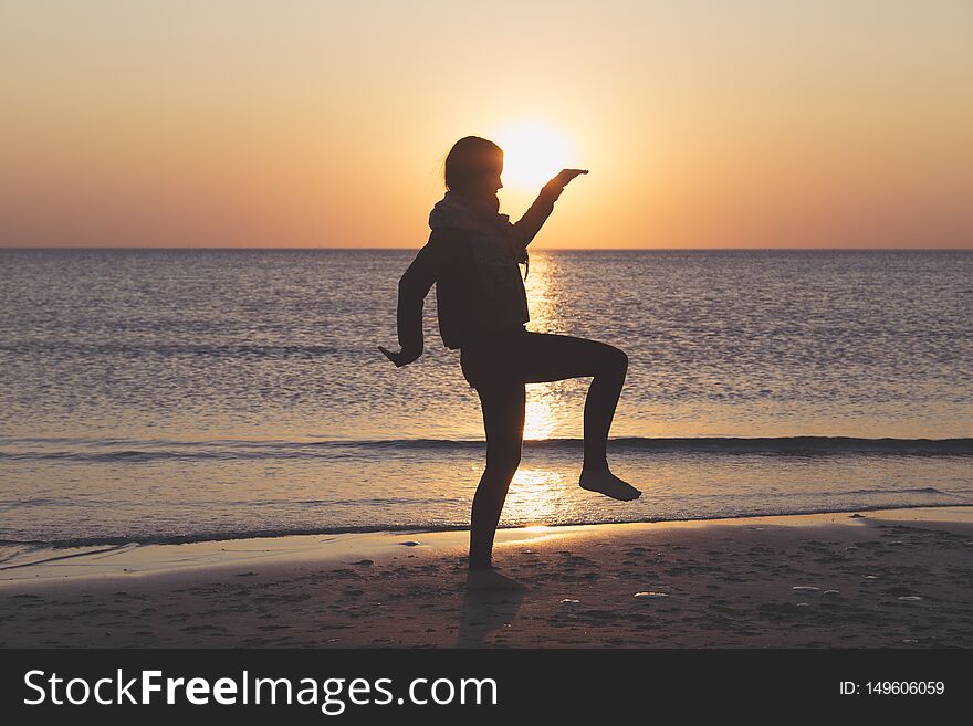Sunset over the sea, woman is dancing on the beach