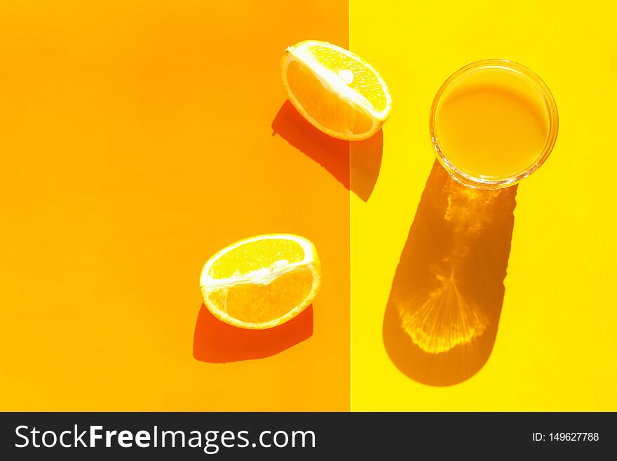 Glass of freshly squeezed citrus juice with pulp orange wedges on duotone yellow background. Harsh light hard shadows. Pop art 80s