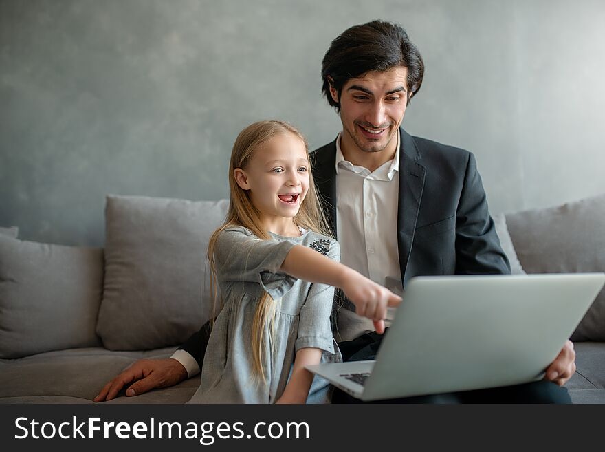 Happy little girl watching a movie on the computer with her father at home