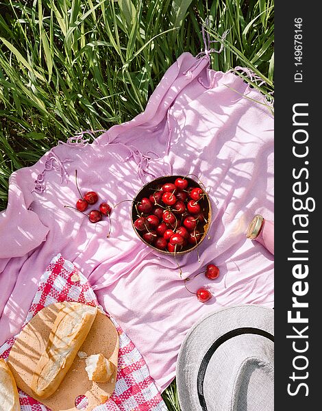 Zero waste summer picnic on the with cherries in the wooden coconut bowl, fresh bread and glass bottle of juice pr smoothie on pink blanket, flatlay