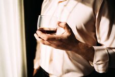 Young Man With Glass On Whiskey Near Window. Man Drinking Whiskey At The Window. Drink Whiskey, Cognac, Close-up. Hand With A Royalty Free Stock Images