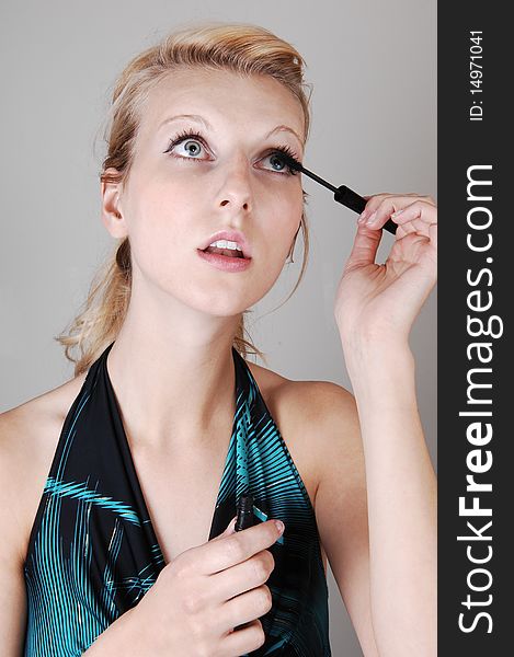 A beautiful blond woman in closeup, doing her makeup and fixing her
eyelashes, looking up, for light gray background. A beautiful blond woman in closeup, doing her makeup and fixing her
eyelashes, looking up, for light gray background.