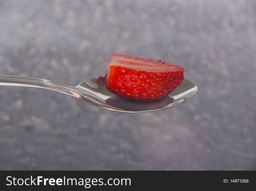 Single red strawberry half on silver spoon. Single red strawberry half on silver spoon