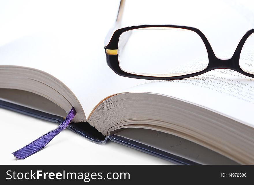 Reading glasses on an open book, closeup on white background. Reading glasses on an open book, closeup on white background