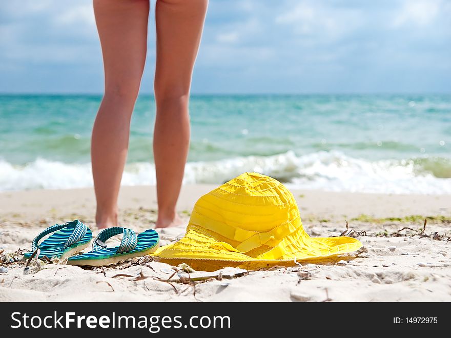 Flip-flop, hat and woman on the beach near sea. Focus on hat