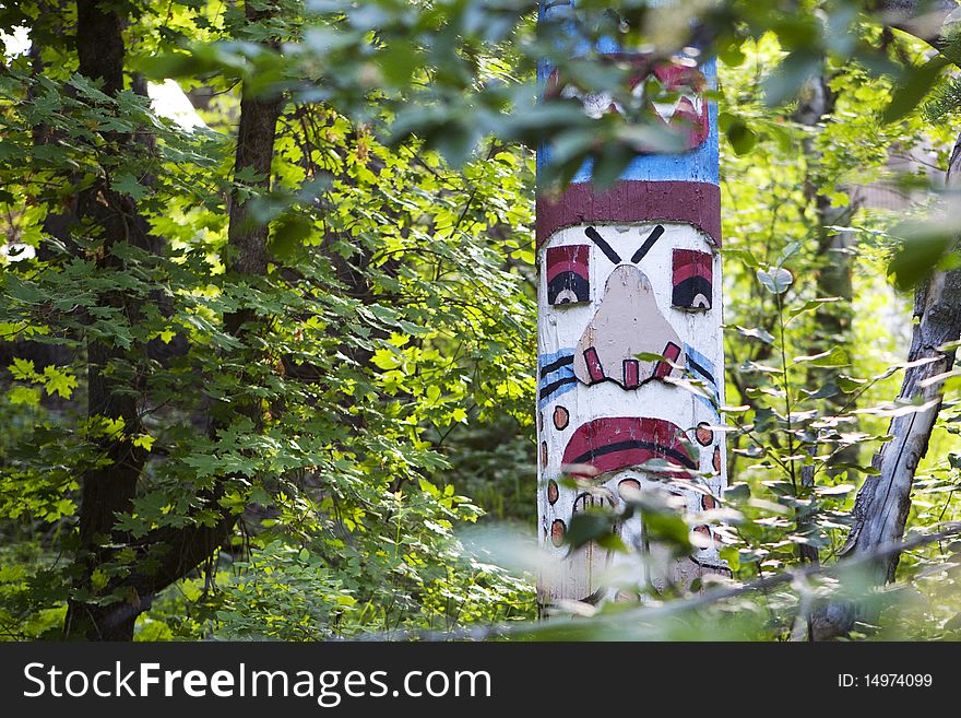 A colorful, painted totem pole amongst the trees in a green forest. A colorful, painted totem pole amongst the trees in a green forest.