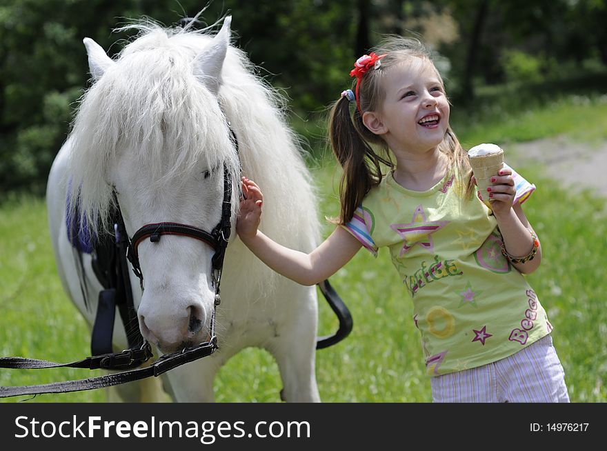 Small white horsy and the little girl with ice-cream, a green lawn. Small white horsy and the little girl with ice-cream, a green lawn