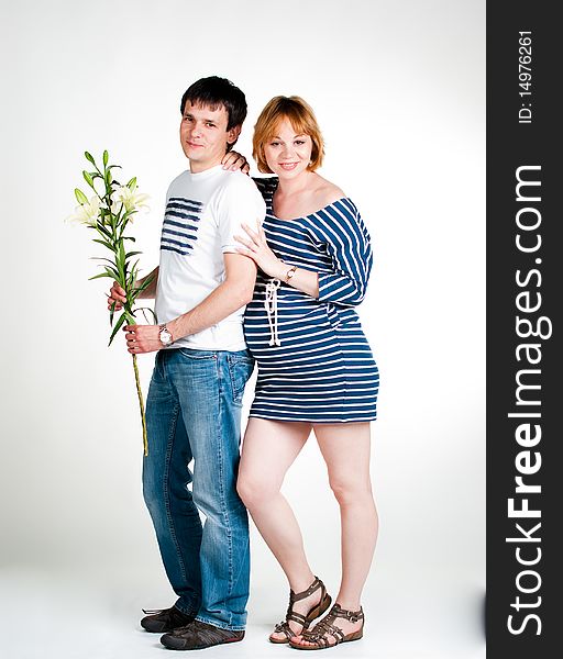 Young beautiful couple dressed in blue and white expecting a baby, with a white lily, symbol of purity. Young beautiful couple dressed in blue and white expecting a baby, with a white lily, symbol of purity