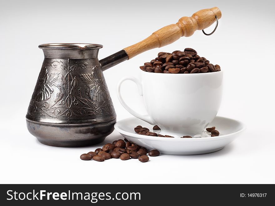 Coffee grains in a white cup and disseminated about a coffee pot on a light background