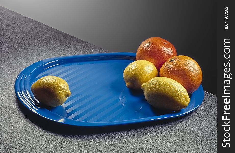 Three lemons and two oranges over a blue plastic tray. Three lemons and two oranges over a blue plastic tray