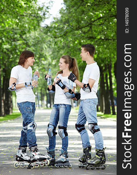 Three young skaters are drinking water in the park. Three young skaters are drinking water in the park