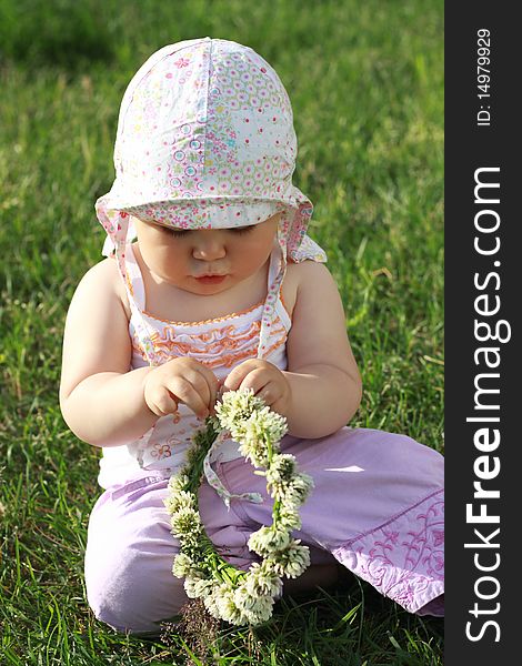 Baby girl sitting on the grass and holding a clover wreath in her hands. Baby girl sitting on the grass and holding a clover wreath in her hands