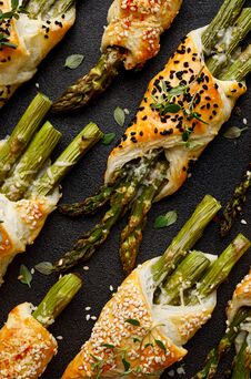 Baked Green Asparagus In Puff Pastry Sprinkled With Sesame Seeds, Nigella Seeds And Fresh Thyme On A Black Background, Close-up, T Stock Image