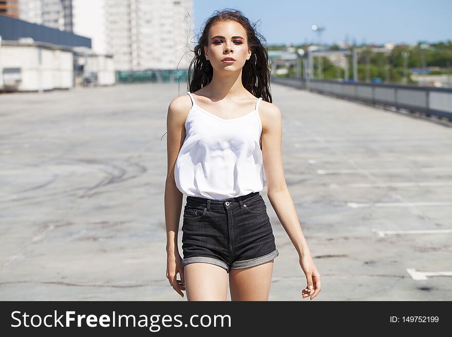 Portrait of a pretty young brunette model in white summer blouse and jeans walking on summer street, outdoors. Portrait of a pretty young brunette model in white summer blouse and jeans walking on summer street, outdoors