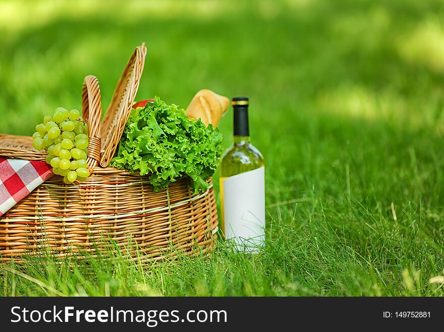 Wicker basket with blanket, wine and food on green grass in park. Summer picnic