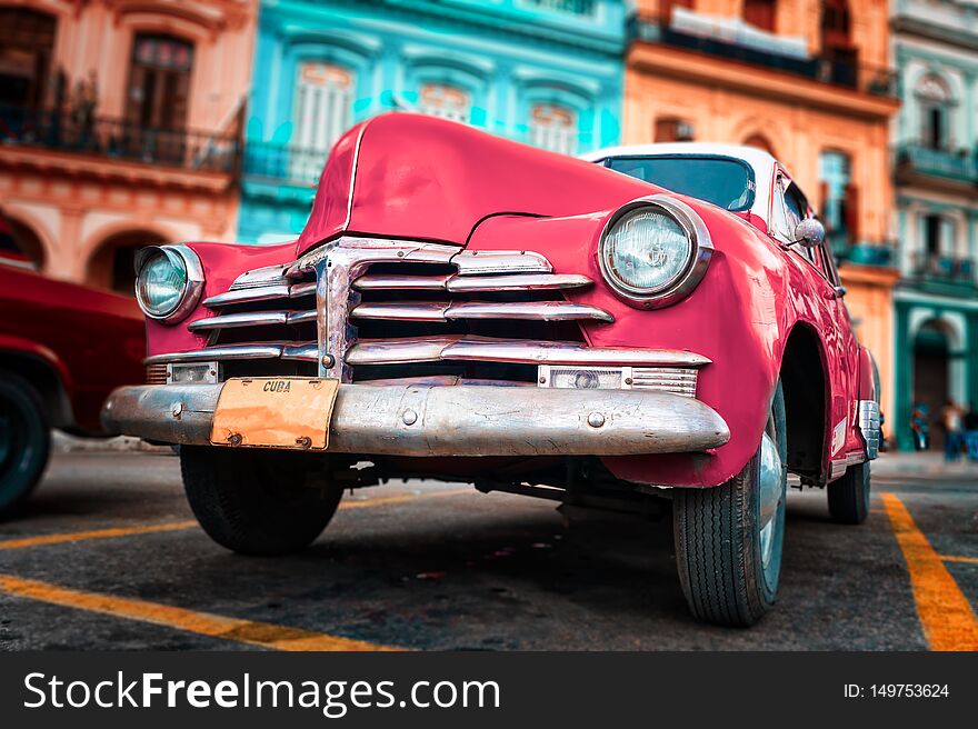 Old car painted hot pink and colorful buildings in Havana