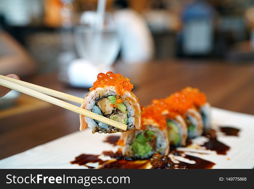 Salmon Roll - A plate of grilled salmon roll with avocado and foie gras, topped with ikura roe and sweet sauce on blurred backgrou