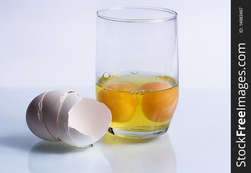 Two broken eggs in a glass and shells on a blue background