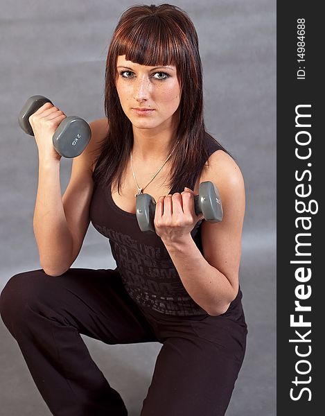 Young woman lifting weights on grey background