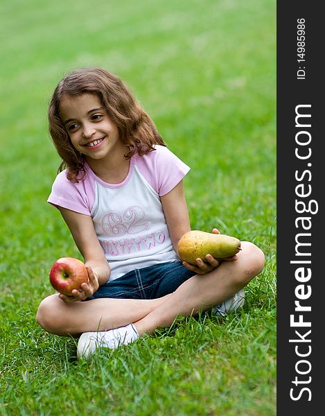 Portrait of a preteen girl with an apple and a plum in her hands and green grass in the background. Portrait of a preteen girl with an apple and a plum in her hands and green grass in the background