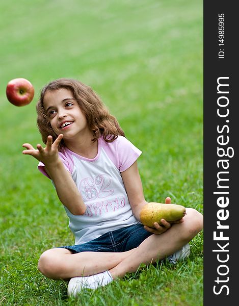 Portrait of a preteen girl trowing apple in the air and with a plum in her other hand and green grass in the background. Portrait of a preteen girl trowing apple in the air and with a plum in her other hand and green grass in the background