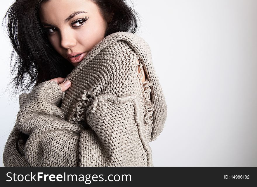 Portrait of Beautiful young brunette in a woollen sweater pose on a grey background in studio. Photo with copyspace.