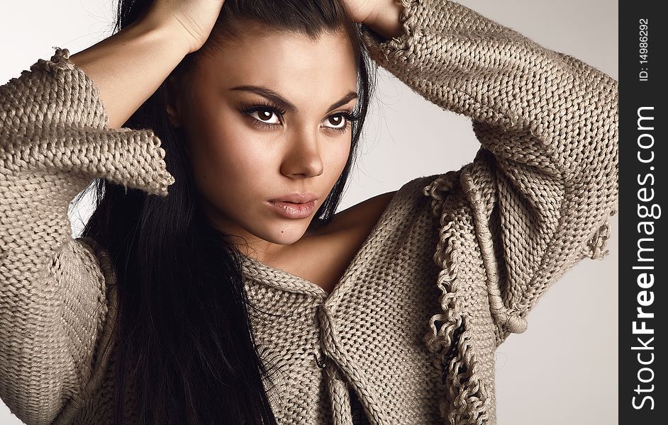 Portrait of Beautiful young brunette in a woollen sweater pose on a grey background in studio. Fashion Photo.