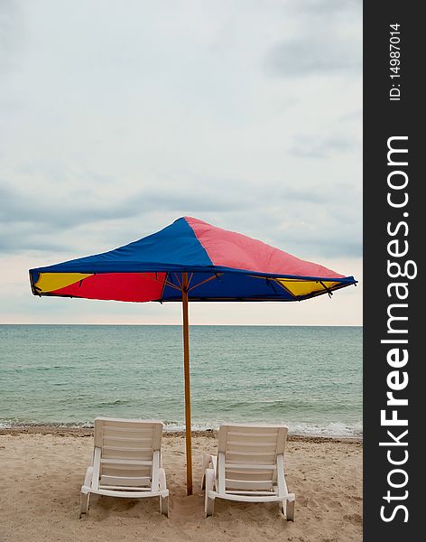 Two beach chairs and umbrella on the sea. Vertical shot