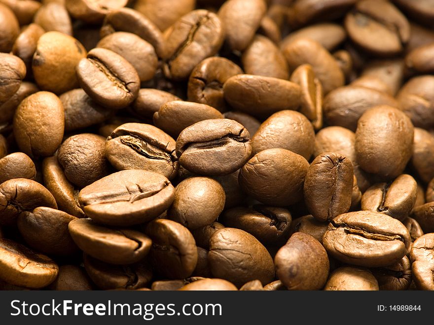 A closeup, macro view of a pile of whole, roasted coffee beans.