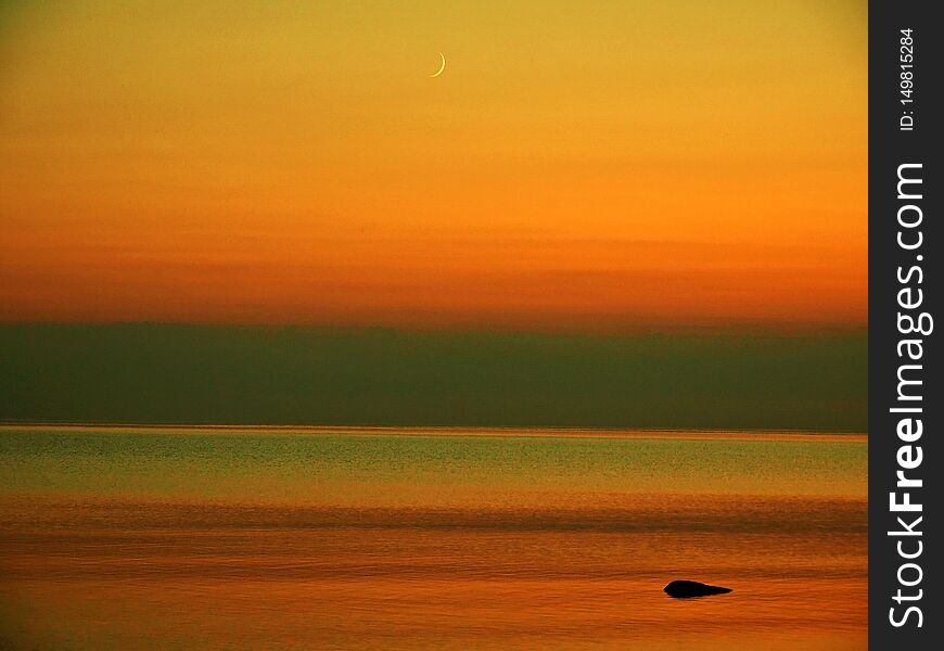 Orange sky after sunset,nMoon set over sea stone coast,nNature reserve. Orange sky after sunset,nMoon set over sea stone coast,nNature reserve.