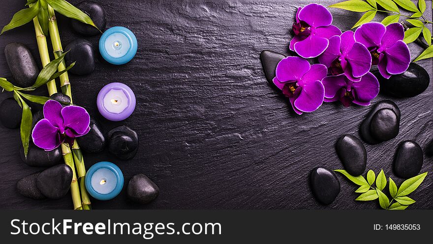 Spa.Group of black stones with purple orchid flowers, bamboo leaves and scented candles on a dark background. Spa.Group of black stones with purple orchid flowers, bamboo leaves and scented candles on a dark background