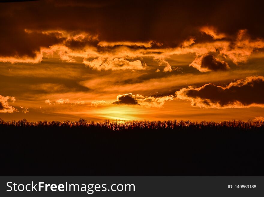Dramatic cloudy orange sunset in the countryside over a line of trees. Dramatic cloudy orange sunset in the countryside over a line of trees