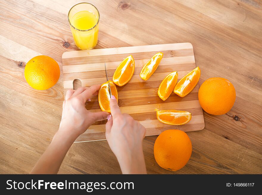 Cooking, food and concept of veganism, vigor and healthy eating - close up of female hand cutting orange on slices.