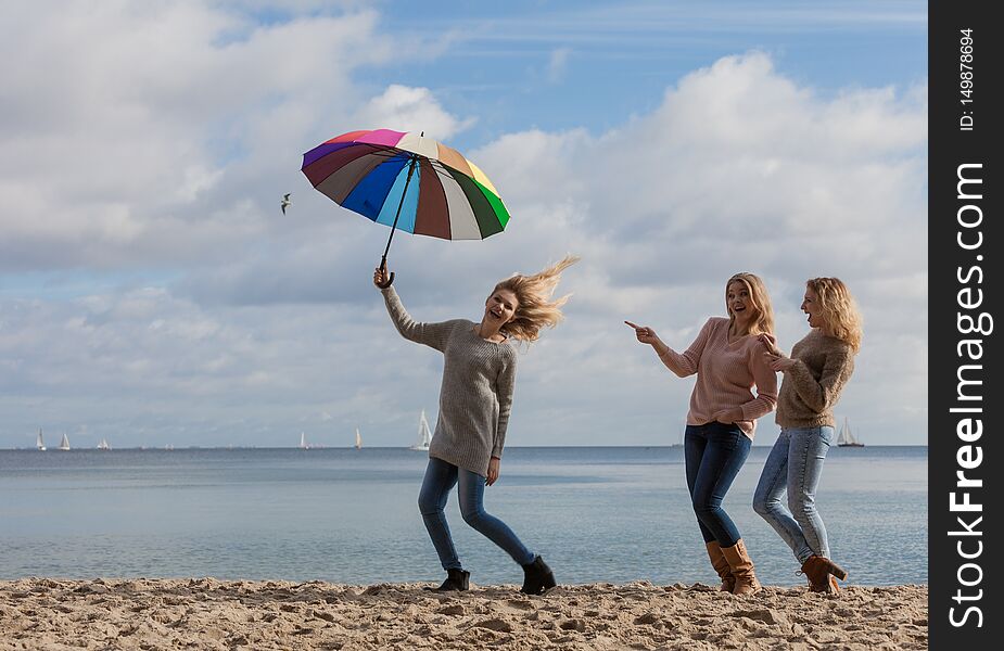 Female jumping with colorful umbrella her two friends are making fun of her laughing and looking. Female jumping with colorful umbrella her two friends are making fun of her laughing and looking