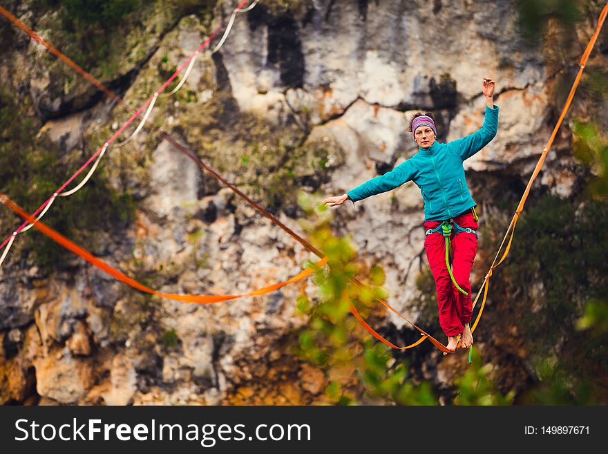 A woman is walking along a stretched sling. Highline in the mountains. Woman catches balance. Performance of a tightrope walker in nature. Highliner on the background of thunderclouds. Fall athlete