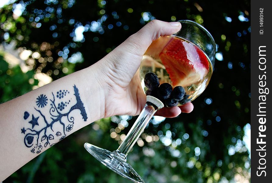 A glass of white sangria in a female's hand with a tree tattoo on her arm.