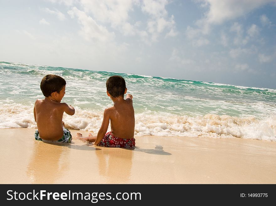 Two boys playing at the sea sitting on the sand