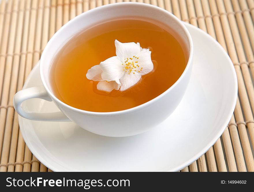 A white cup of tea on a tray with jasmine flower. A white cup of tea on a tray with jasmine flower