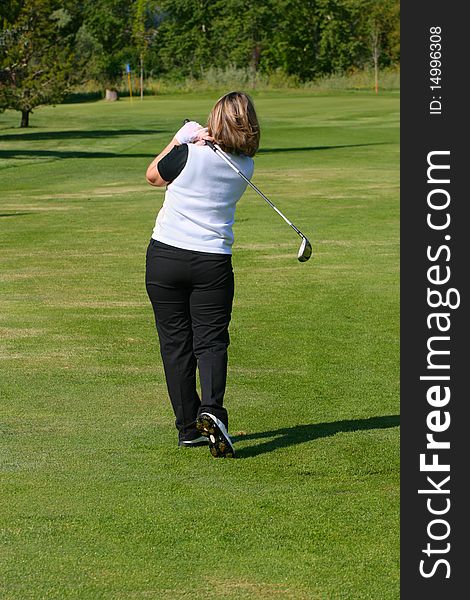 Blond female golfer following her shot from the fairway