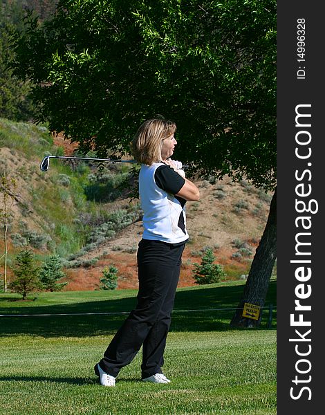 Blond female golfer following her ball down the fairway