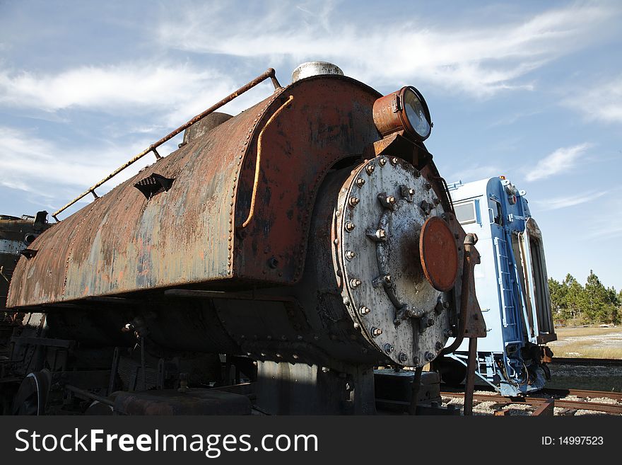 Closeup photo of an old steam locomotive engine with a train car in the background