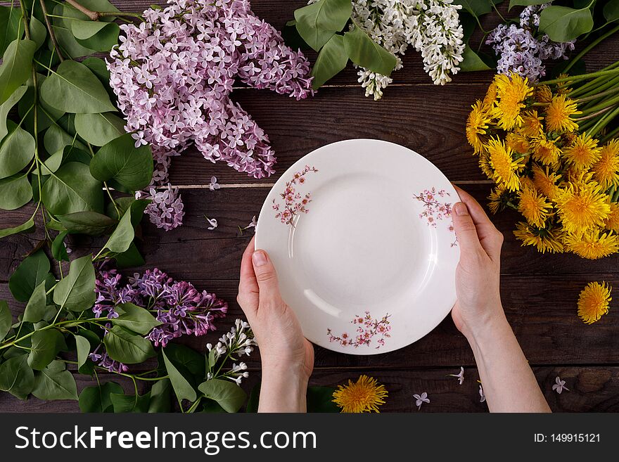 Plate and decor of flowers on the background of vintage wooden planks. Vintage background with flowers of dandelion and lilac and a place under the text. View from above. Flat lay. Cutlery. Vintage