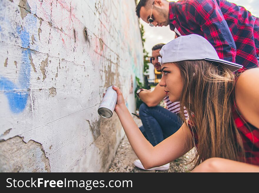 Three urban people are having fun together, drawing grafitii on the wall. Three urban people are having fun together, drawing grafitii on the wall