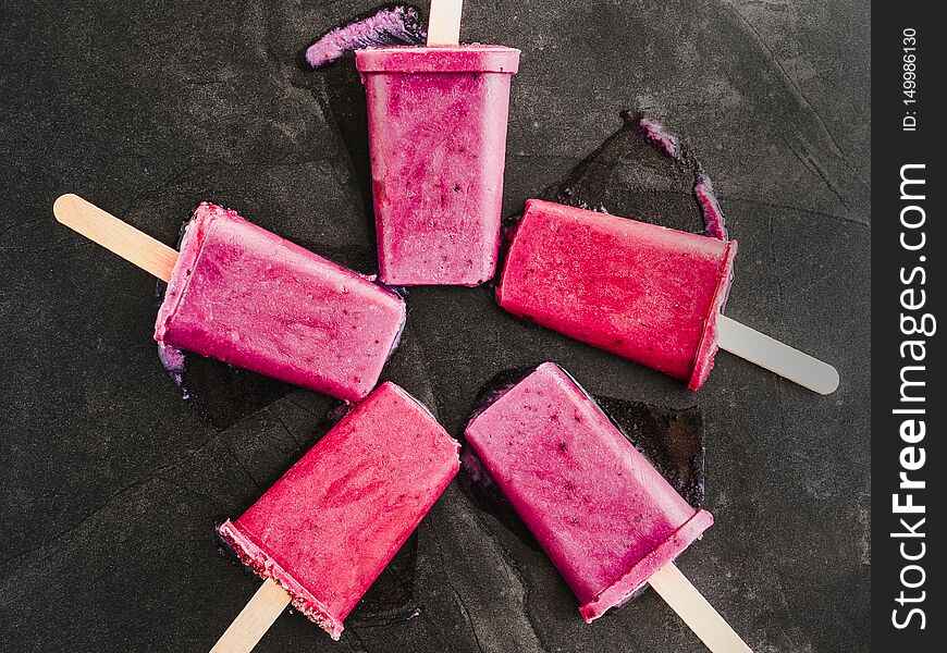 Bright, fruity fuchsia ice cream with wooden sticks on a dark surface. Close-up, top view. Tasty and healthy food concept. Bright, fruity fuchsia ice cream with wooden sticks on a dark surface. Close-up, top view. Tasty and healthy food concept